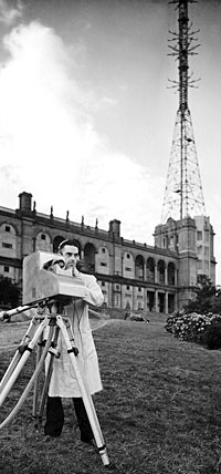 1930s cameraman outside a Victorian building on a hill