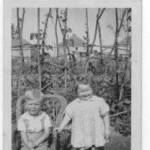 Peter with cousin Anne in July 1944. Italian Prisoner of War Camp in background behind the runner beans. Ash near Aldershot.