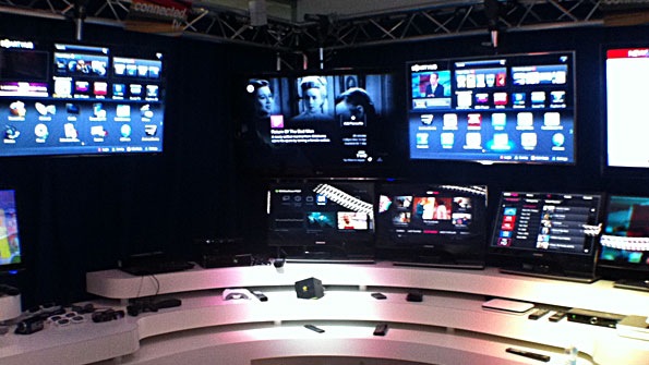 Bank of TVs and monitors over an arena in which remote controls site, watching.