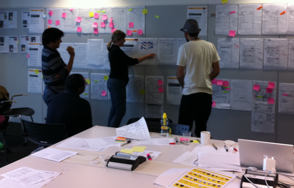 A meeting, poring over designs on the wall