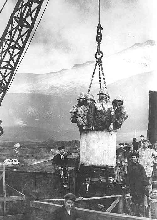 Workmen being lifted by a steam crane.