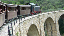 Narrow gauge train and railway Pelion Greece© BBC. Exactly a century ago the little train of Pelion started. The 'Volos - Milies' line was designed by Evaristo de Kiriko (father of the famous artist). Today many years after the closure of the line, the train has started functioning again. The journey is fascinating passing through green valleys, gorges, small tunnels and crossing arched bridges. It operates on the weekends travelling from Milies to Lehonia.