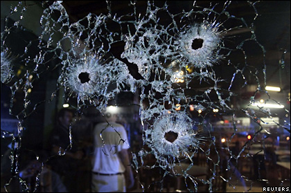 People stand behind the bullet-riddled window of a restaurant in Mazatlan