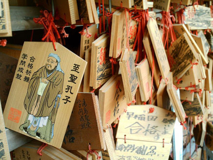 Wooden prayer tablets with images hung with red string on shrine gate.