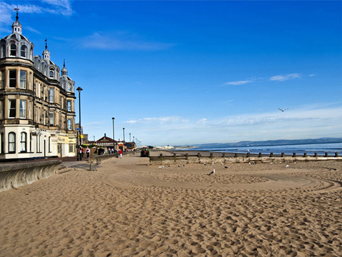 A large empty beach with an ornate Victorian tenement to the left of frame.