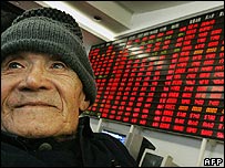 Chinês em frente a placar eletrônico mostrando preços de ações