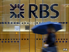 Person with umbrella walks past RBS building