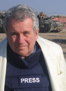 Presenter Martin Bell stands in front of a tank, wearing a bulletproof vest with the word PRESS on it