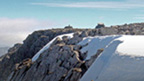 View across rocks, snow and ice to the flat summit of Ben Nevis.