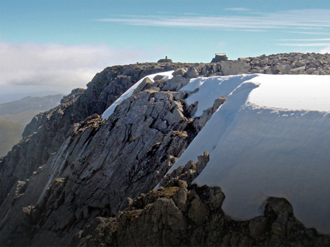 View across rocks, snow and ice to the flat summit of Ben Nevis.