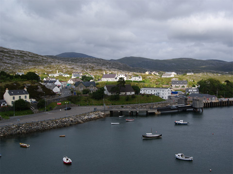 Colour view across bay to modern, concrete pier with a number of cottages and other buildings behind.