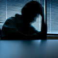 A person in shadow, sitting with their head in their hands, signifying depression