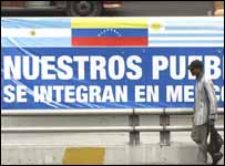  Homem caminha em frente a cartaz do Mercosul
