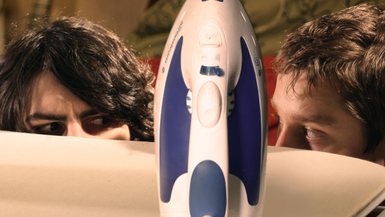 Gareth Aldon (Steve) and James Kristian (Tom) eye each other behind an iron and ironing board.