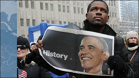 January 2009, Chicago. A man holds a local newspaper image of Barack Obama while watching live coverage of the new President's inauguration ceremony. Credit: Eyevine