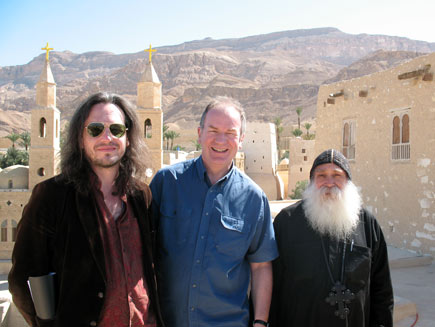 Nicholas Buxton, Stephen Shipley and Father Ruwais smile at the camera among the buildings of St Antony's Monastery with the Egyptian mountains in the background