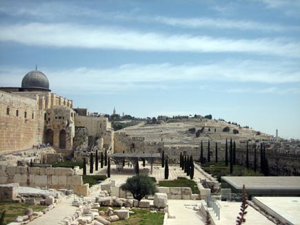 The silvery dome of the Al Aqsa mosque on the left, looking out towards the Mount of Olives in the background, with old, tumbledown walls of white stone blocks in the foreground