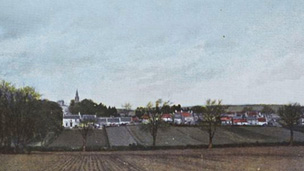 Hand-tinted view across gently rolling, ploughed fields to a village beyond. A church spire rises to the left of frame.