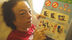 Liz Carr examines the in-flight safety card, which shows how to adopt the brace position
