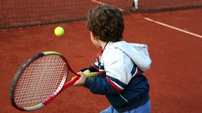 Young boy hitting a backhand on a tennis court.