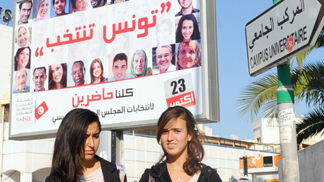 Tunisian students pass in front of a poster of election candidates 