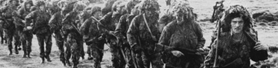 A line of British soldiers in camouflage advancing during the Falklands War