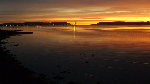 Calm shoreline at sunrise, distant oil rig on Cromarty Firth