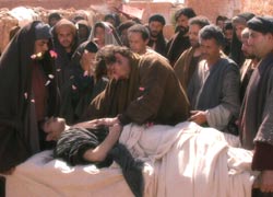 Jesus laying his hands on the dead body as crowds look on