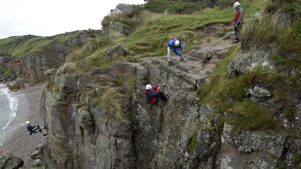 Rachel Guest abseils down the cliff while Andy Simpson rock climbs in the distance.