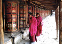 Robed Tibetan monks at Little Tibet, Xiahe, Guangshu, China, turning huge prayer wheels mounted along a wall