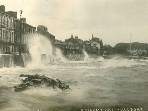 Black and white view of Stuart Street, Millport showing large storm waves breaching the sea wall.