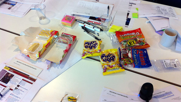 Design mockups, documents, and sugary sweets scattered across a white meeting room table.