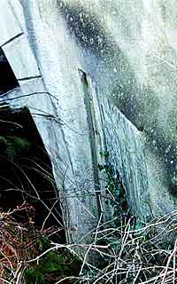 A memorial stone hidden from view on the side of a bridge