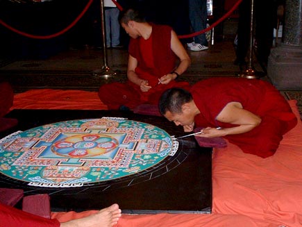 Monks seated around the mandala, now working on the beginnings of the outer border