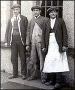 Three men outside a house in Biggar, wearing their work overalls